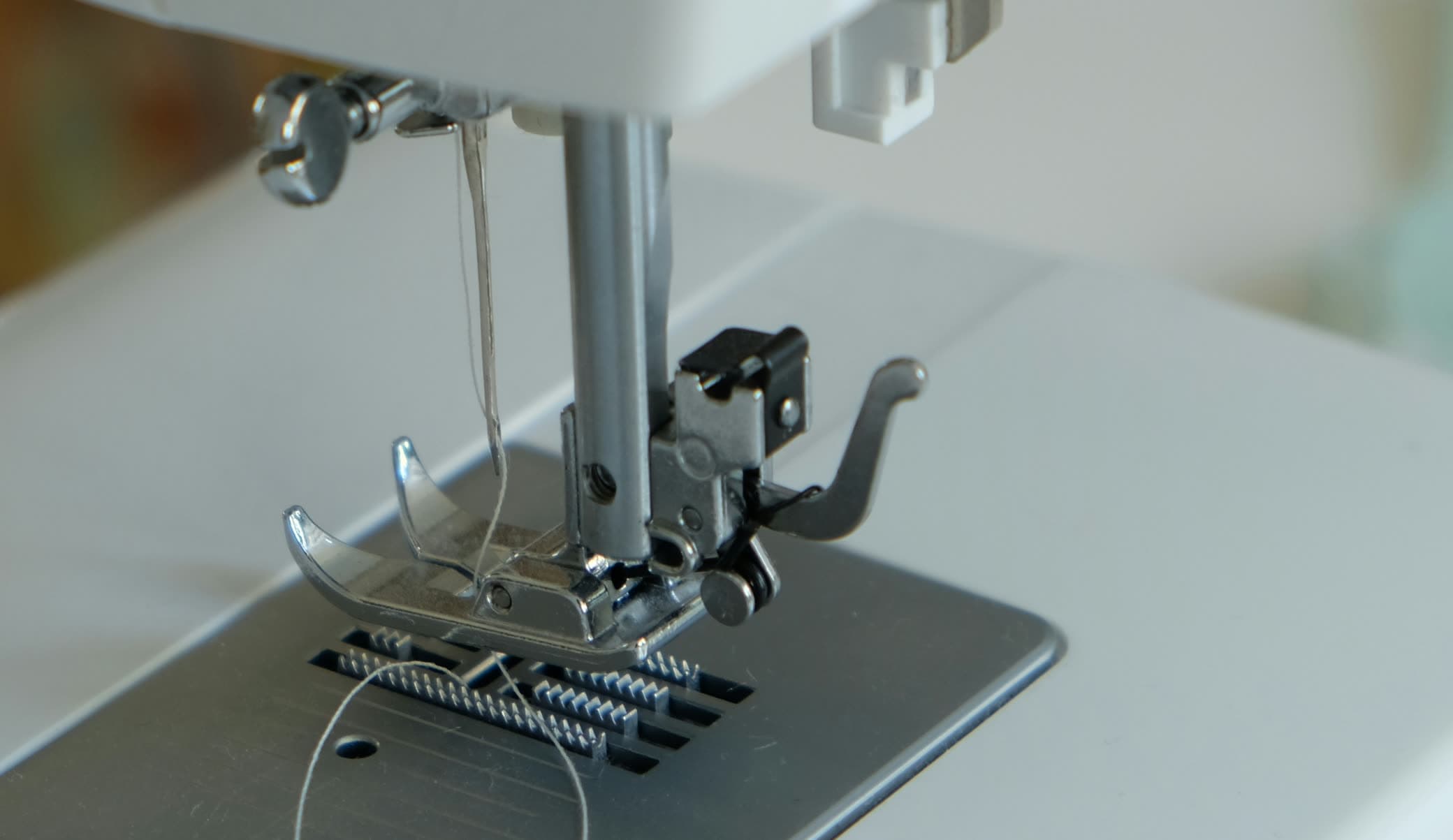 Close do calcador abaixado e da agulha com a linha passada numa máquina reta doméstica